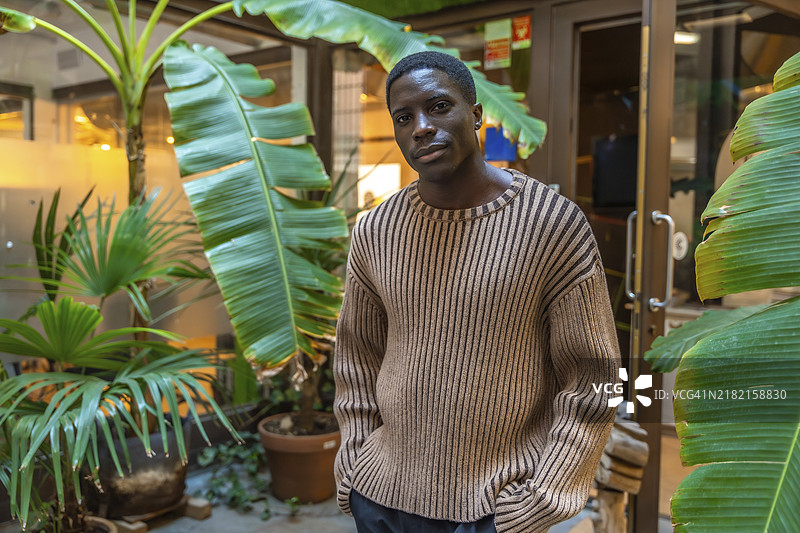 一位休闲打扮的非洲年轻男子站在共享办公空间外。图片素材