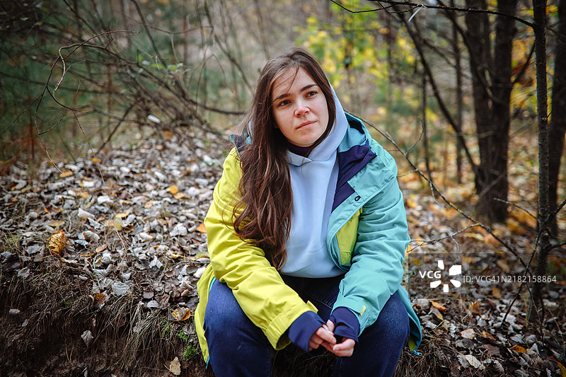 一位女性坐在秋天的森林中，她的思绪和情感在大自然的宁静中得以映照。图片素材