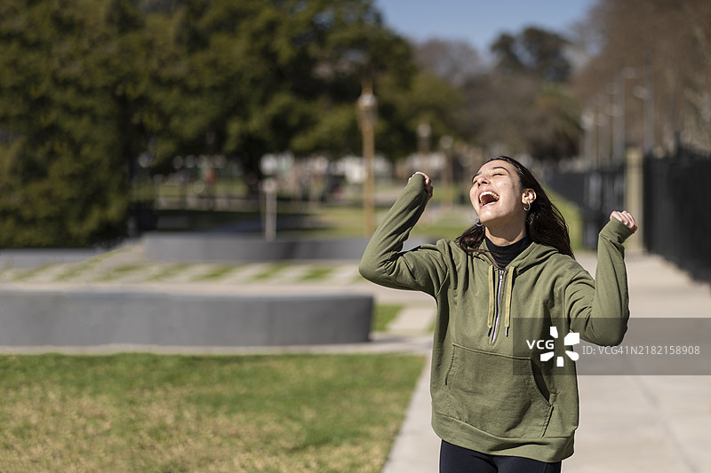 年轻女孩穿着运动服在公园里庆祝，微笑着尖叫，双臂高举。图片素材