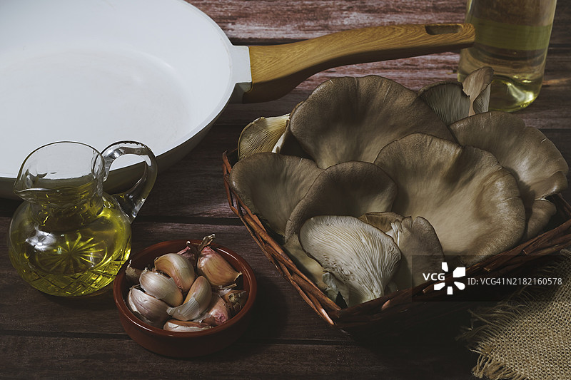野蓟蘑菇（Pleurotus eryngii）与烹饪食材大蒜和橄榄油放在一个柳条篮子里图片素材