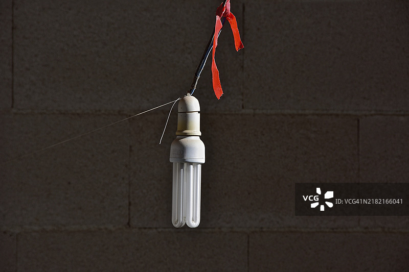 节能灯泡悬挂在绳子上，背后是石墙图片素材