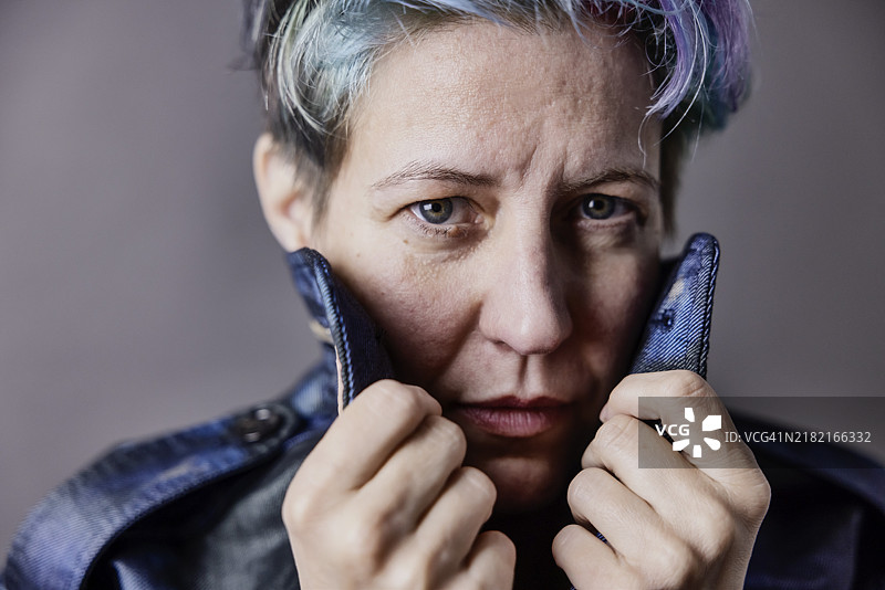 一位染发的中性风格女性拉起她牛仔夹克的领子，肖像照图片素材