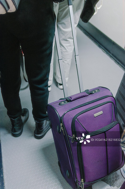 在机场航站楼中走动的紫色行李箱的人，适合旅行、旅游和过境主题图片素材