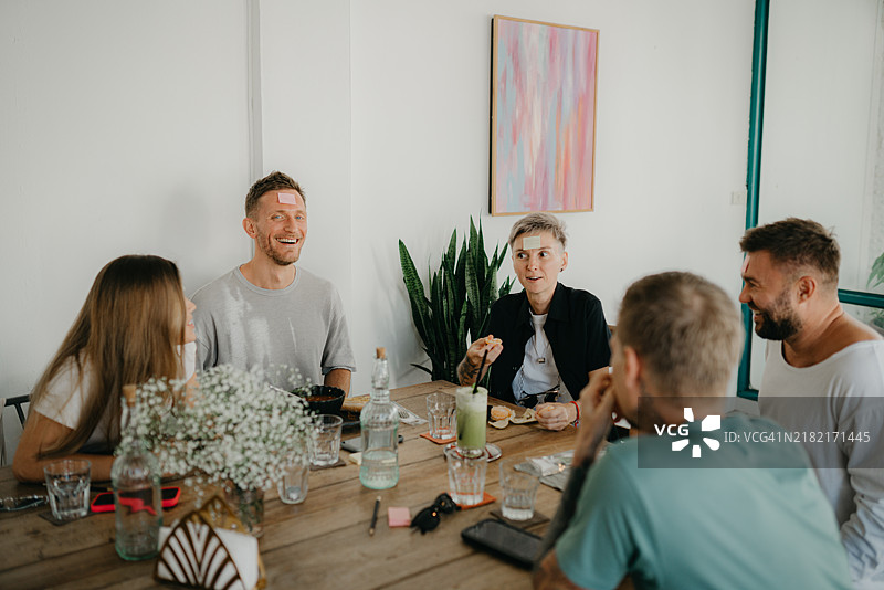 朋友们聚在一起吃饭并玩“我是谁”的游戏图片素材