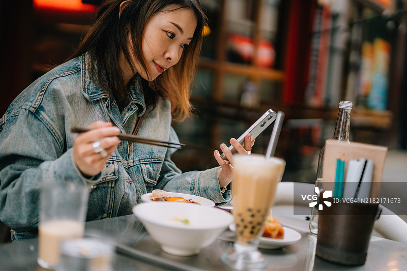 年轻的亚洲女性在台湾餐厅用餐时使用智能手机图片素材