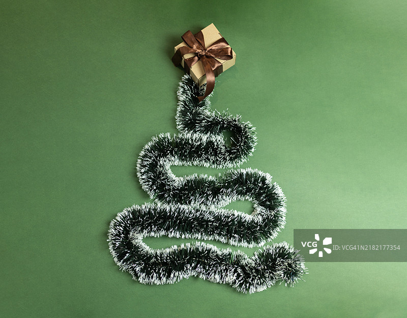 圣诞花环以圣诞树的形状嵌套，旁边有一个系着棕色蝴蝶结的礼盒图片素材