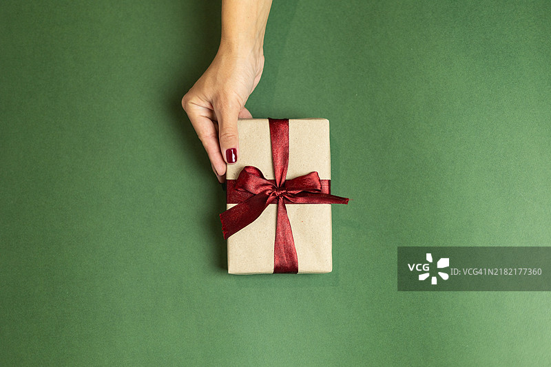 一只涂有酒红色指甲油的女性手握着一个带有酒红色蝴蝶结的礼品盒图片素材