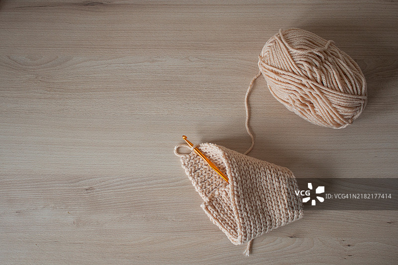 一团米色毛线和一个橙色钩针放在木质表面上图片素材