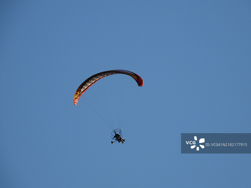 低角度视图的人在晴朗的天空中滑翔伞飞行图片素材