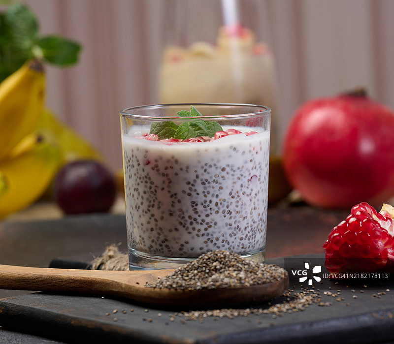 一个装有奇亚籽和酸奶的玻璃杯，旁边放着木勺，甜点中还加入了石榴籽。图片素材