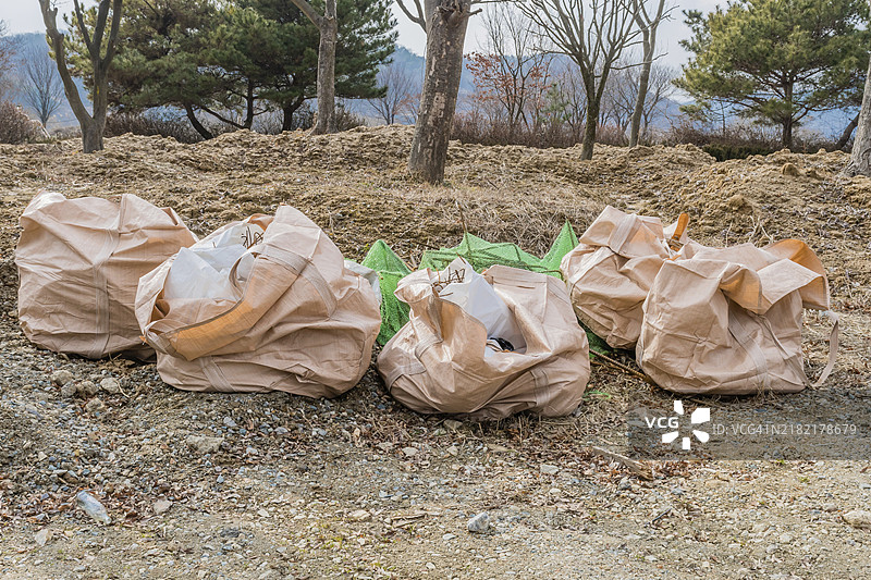 建筑工地前树木下的麻布袋装满垃圾放在地上图片素材