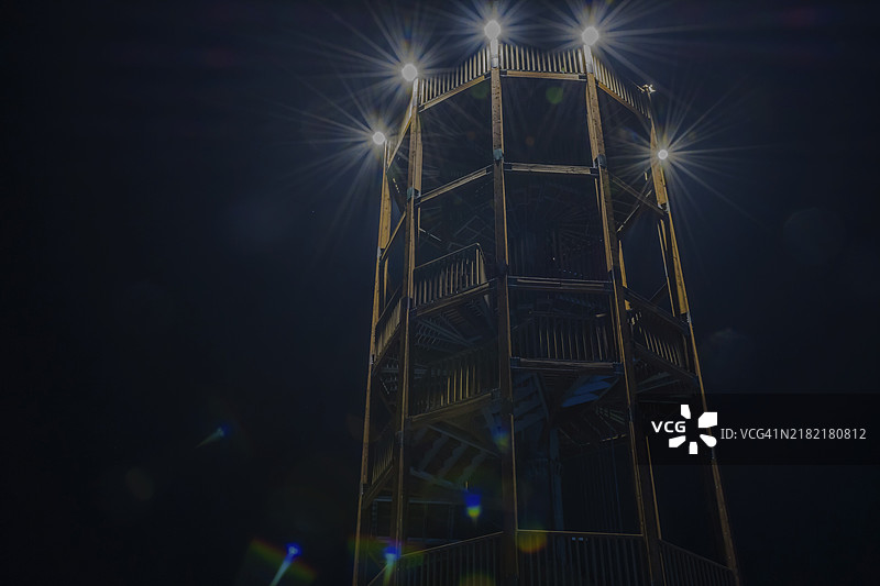 低角度夜景，木制观景塔被安装在上层甲板上的泛光灯照亮，背景是没有星星的夜空，位于韩国。图片素材