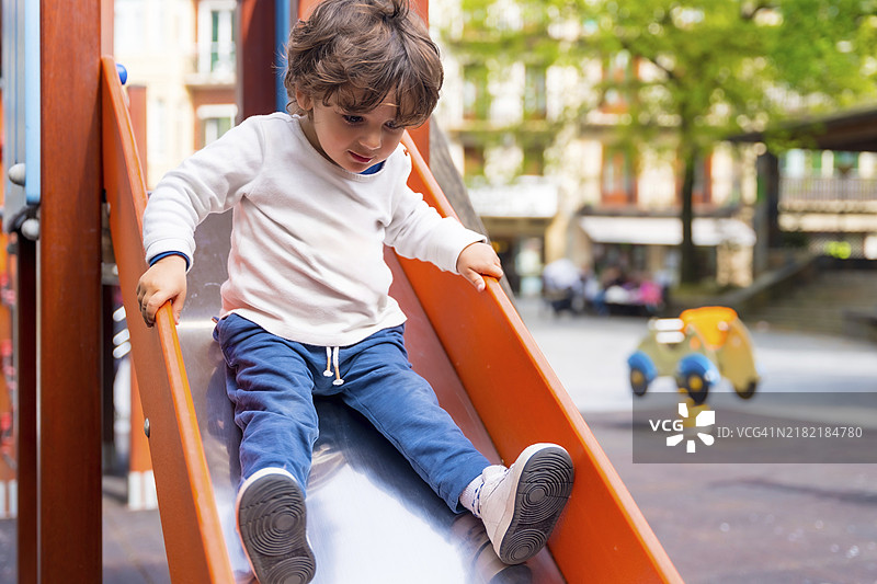 一个小女孩在城市游乐场的滑梯上滑下去图片素材
