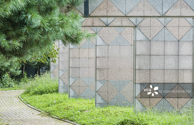 韩国公园中，砖砌人行道穿过一系列带有三角形图案的墙壁，周围是林木。图片素材