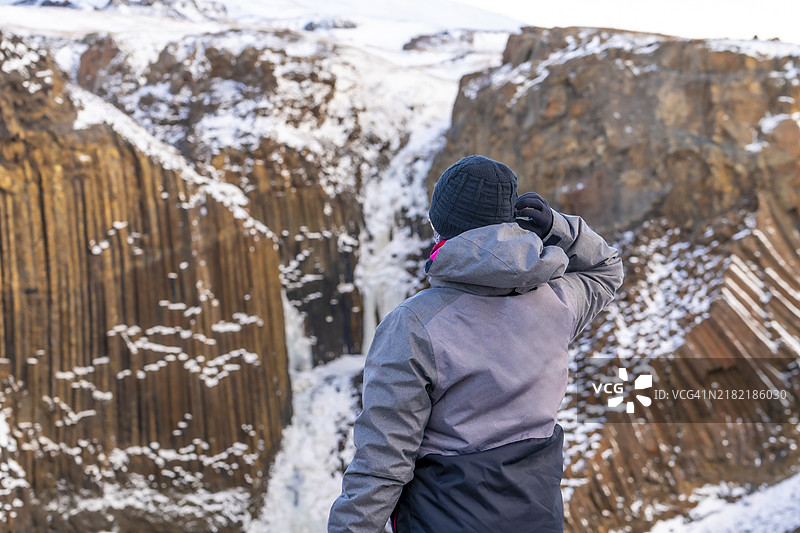 从背后看着冰岛冬季冰封的亨吉福斯瀑布的女人。冬季旅游在这个美丽的国家。图片素材