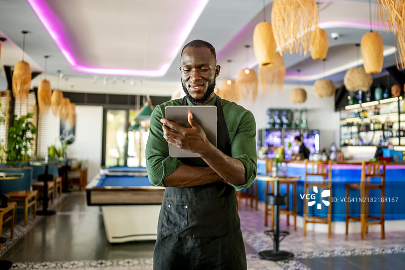 微笑的调酒师在时尚酒吧环境中使用数字平板电脑图片素材