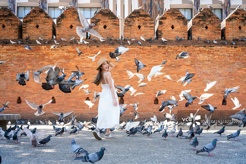 快乐的亚洲女性在清迈塔佩门的历史砖墙前被飞翔的鸽子包围图片素材