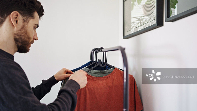 年轻男子在家中查看挂在架子上的T恤衫图片素材