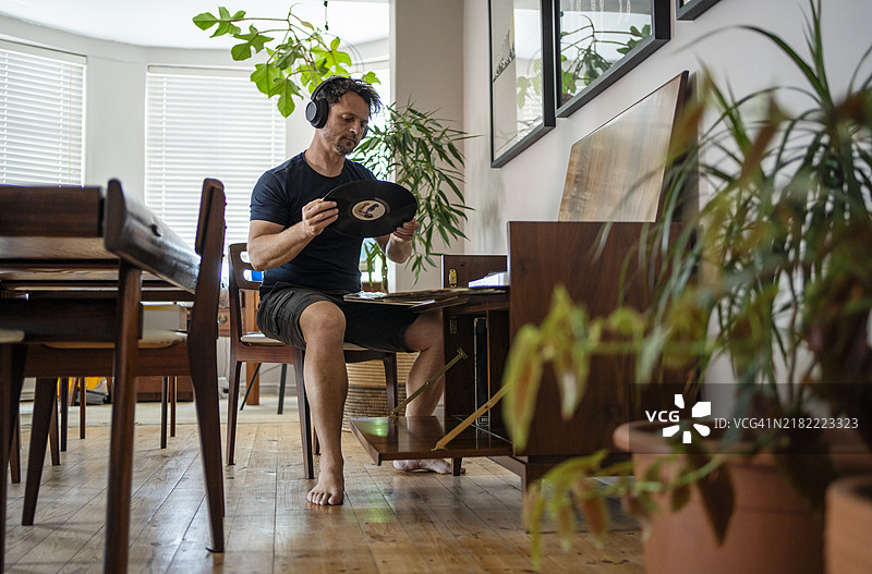 成熟男性在家中戴着耳机听唱片图片素材