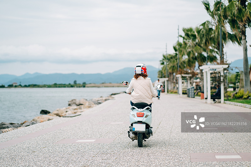女性骑摩托车旅行。头戴安全帽的女性从后方视角骑乘摩托车。图片素材