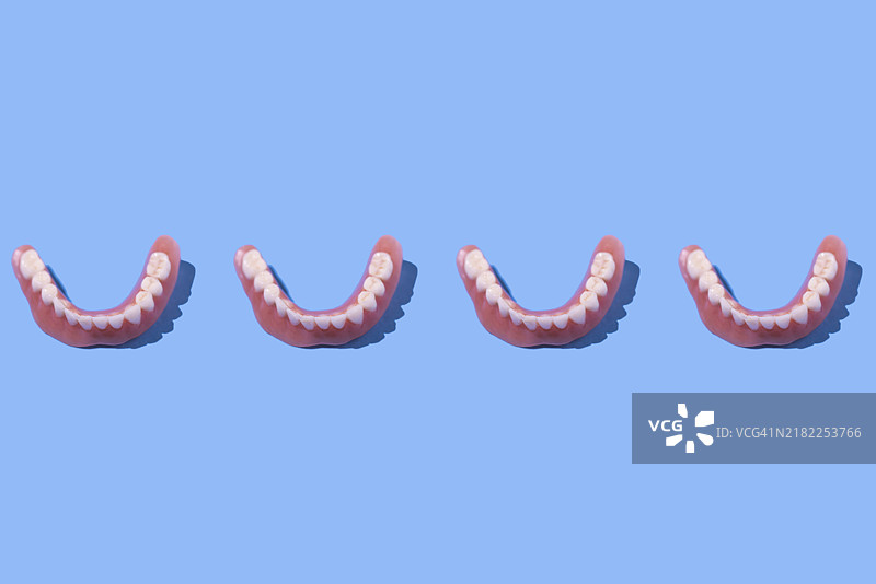 蓝色背景上的下颌义齿模型，整齐排列。牙医、植牙、牙科、诊所和治疗。图片素材