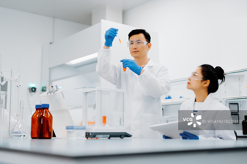 亚洲男性科学家在现代实验室与同事们愉快地工作。他正在使用微量移液器进行测试分析。图片素材