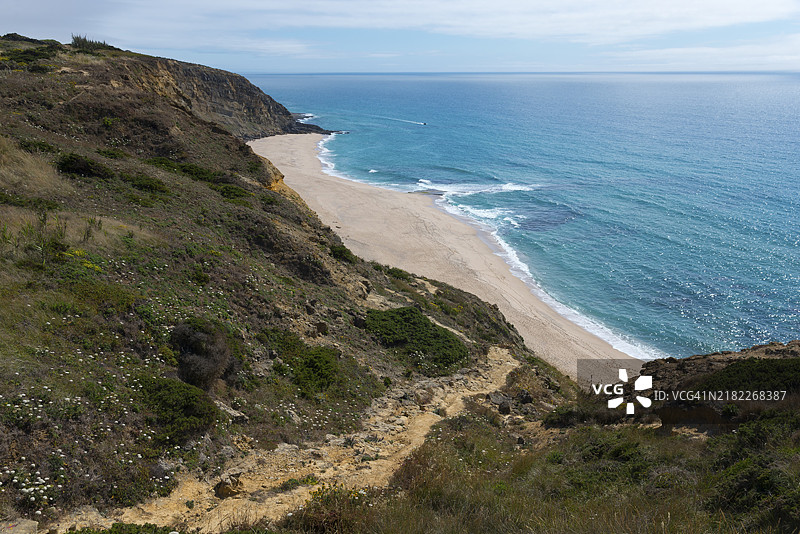 海岸风景，蓝色海洋、悬崖和沙滩在晴朗的天空下，位于葡萄牙里斯本的埃里塞拉维吉亚海滩。图片素材