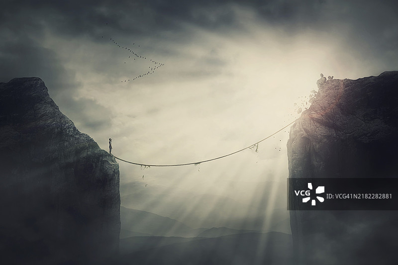 站在悬崖边缘的人决心通过一座古老的松弛绳索桥克服障碍。成功的追求、危险与风险的概念。两座山峰之间的走钢丝，隐喻场景。图片素材
