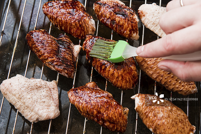 特写镜头：一个人用刷子给油炸鸡翅涂抹油。图片素材
