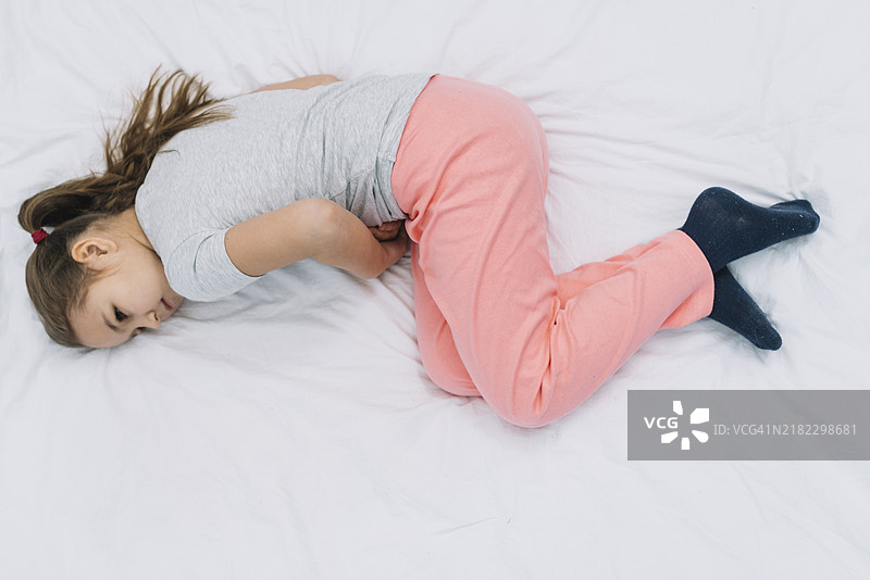 俯视图：女孩躺在床上，腹痛难忍图片素材