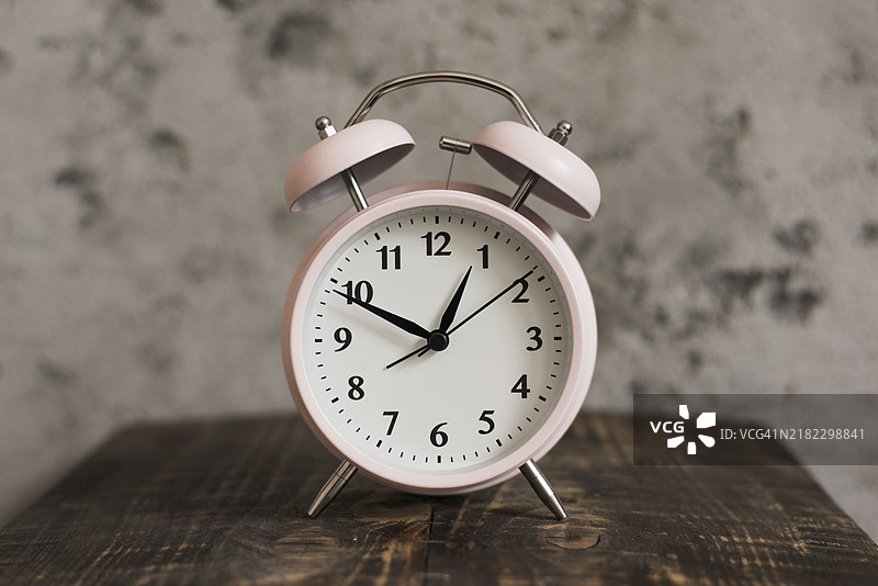 粉色闹钟放在木质桌子上，背景是风化的墙壁图片素材