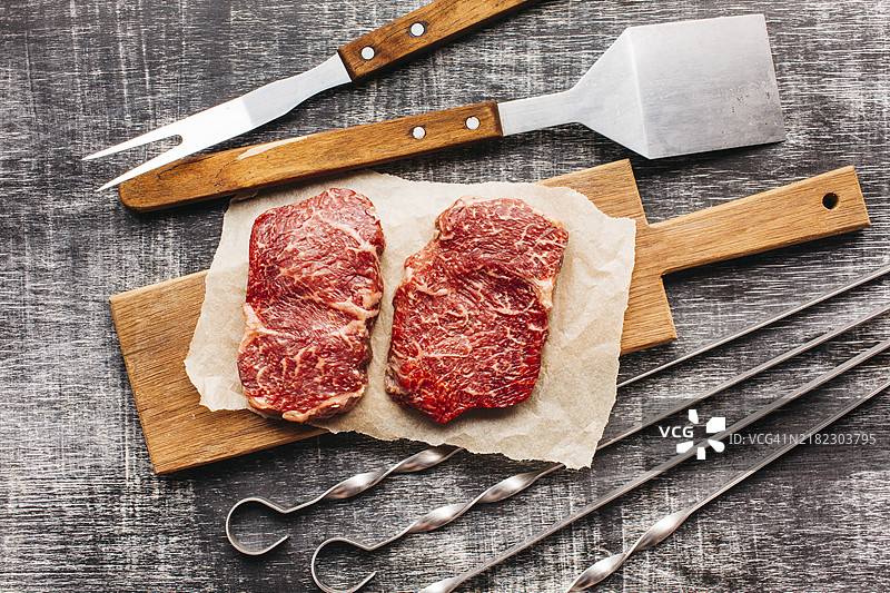 高处视角的生牛排、烧烤工具和木质纹理表面图片素材