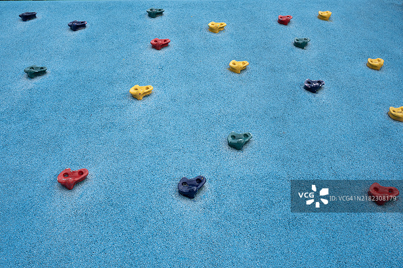 一个蓝色的墙壁上装有一堆五彩缤纷的攀爬把手，位于游乐场的攀爬山上图片素材