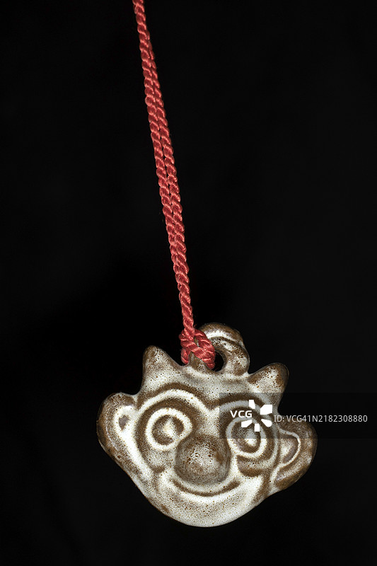 克勒波勒，来自波罗的海丹麦博恩霍尔姆岛的陶瓷吉祥物，挂在红色绳子上，黑色背景的工作室摄影。图片素材