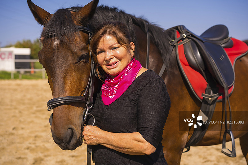 一位成年女性骑在马背上，轻抚一匹棕色马，身穿南美风格的服装。图片素材