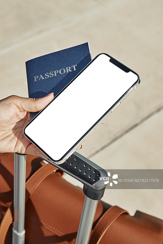 女性在疫情期间手持护照和智能手机，旁边有行李，身处机场。图片素材