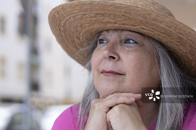 侧面特写，一位戴着帽子、白发的女性沉思地望向地平线。图片素材