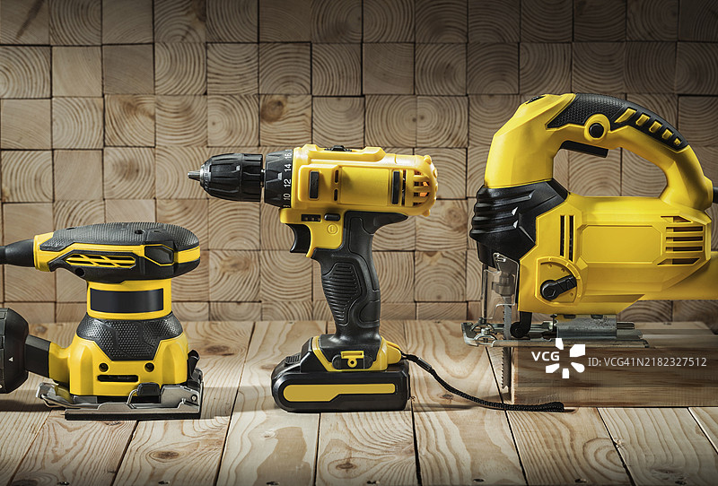 电动有线曲线锯、无绳电钻和木材打磨机放在木质背景上图片素材