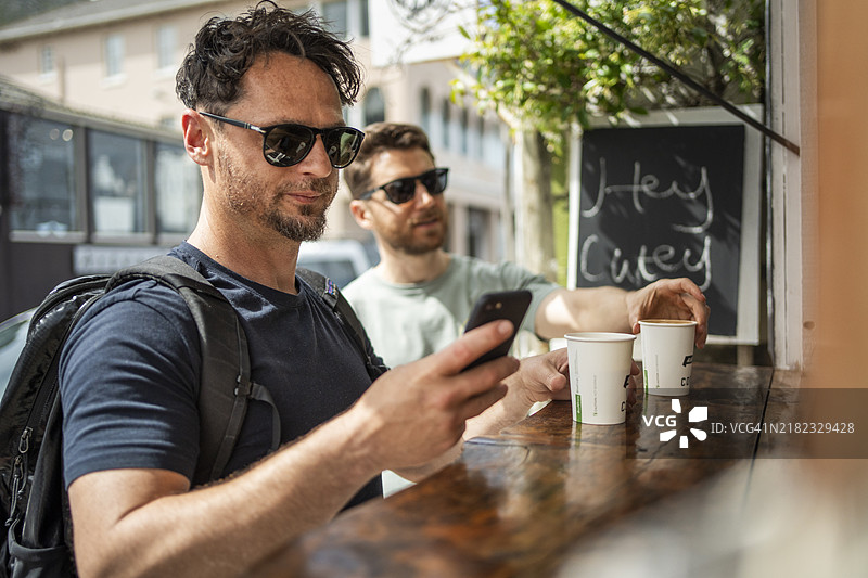 男子在城市小摊与朋友一起用手机购买咖啡图片素材