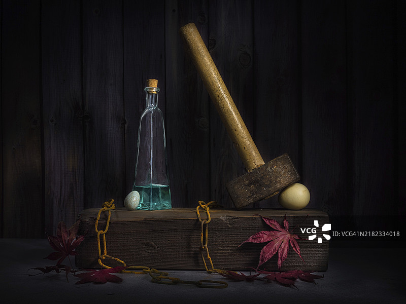 静物画：旧锤子、鸟蛋、生锈的链条和玻璃瓶放在枫叶上的木块上图片素材