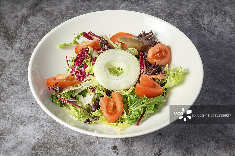 绿色素食沙拉，由绿色叶菜和蔬菜混合而成。俯视灰色石桌上的沙拉。图片素材