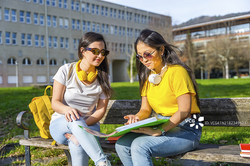 多民族学生戴着耳机坐在校园长椅上看作业图片素材