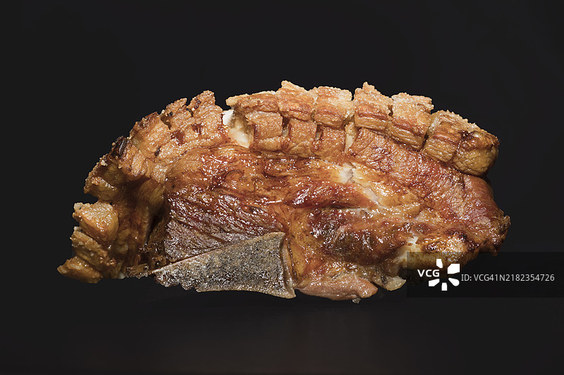 新鲜烤制的带骨五花肉，外皮酥脆，黑色背景的美食摄影图片素材