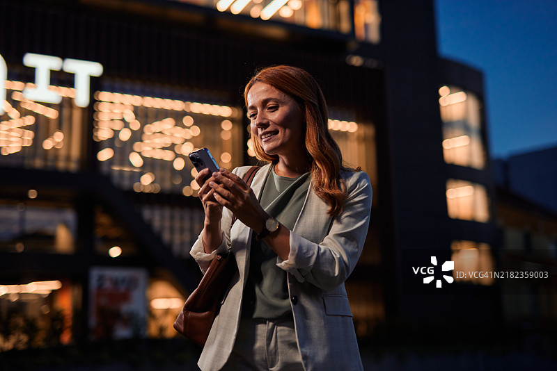 女性在城市夜景中微笑着使用智能手机图片素材