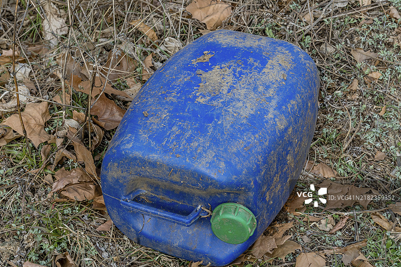 在韩国，周围被叶子环绕的风化蓝色塑料桶，带有绿色盖子。图片素材