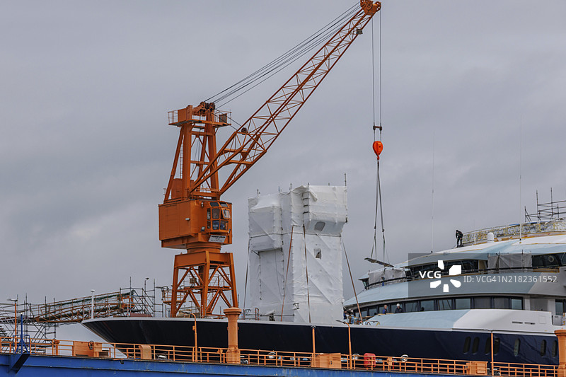 一艘大型船只停靠在船厂，旁边是一座醒目的橙色起重机，德国不来梅哈芬，欧洲图片素材