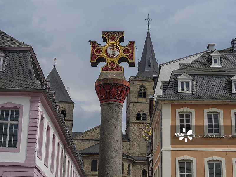 历史建筑和教堂塔楼，前景中有华丽的十字架，阴云密布的天空下，历史房屋的正面与纪念碑在阴沉的天空下，德国特里尔，欧洲图片素材