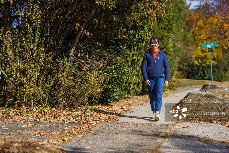 在五彩斑斓的秋季风景中漫步。拉丁裔女性在新泽西州享受宁静的郊区散步。图片素材
