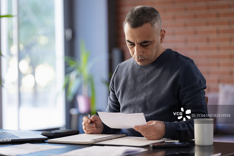 中年男子在家中审阅纸质财务报表图片素材