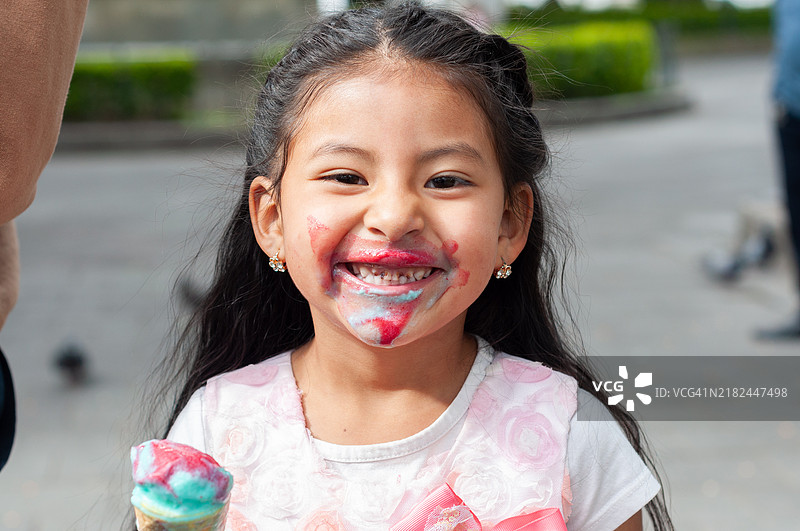 小女孩灿烂地微笑，脸上沾满了甜美的五彩滴液。图片素材